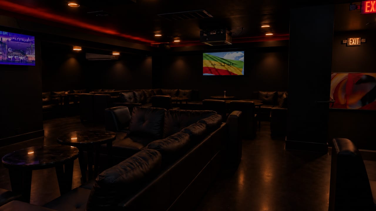 The lounge’s long leather sectional and round tables beneath red ceiling light, with a screen showing the Ethiopian flag on the far wall.